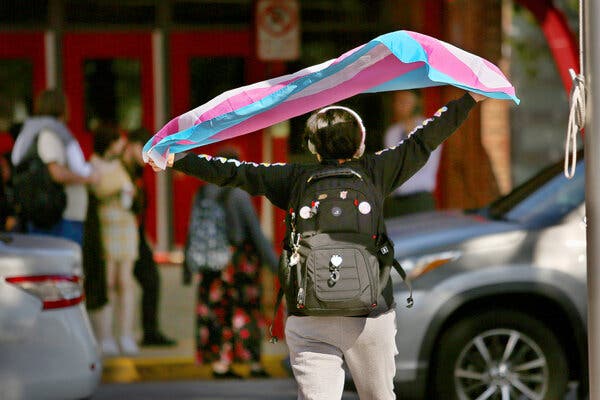 A high school student waves a transgender flag outside their school.