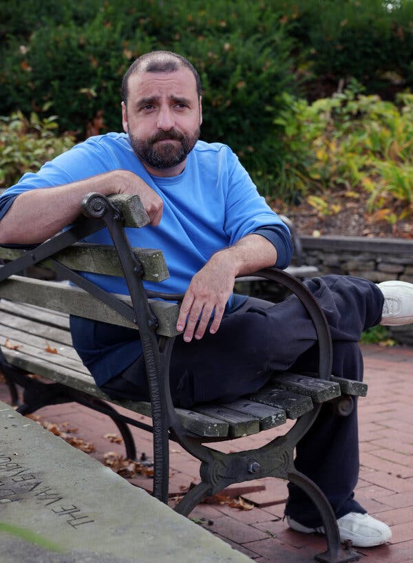 David Krumholtz sits on a park bench, in a blue shirt and dark pants.