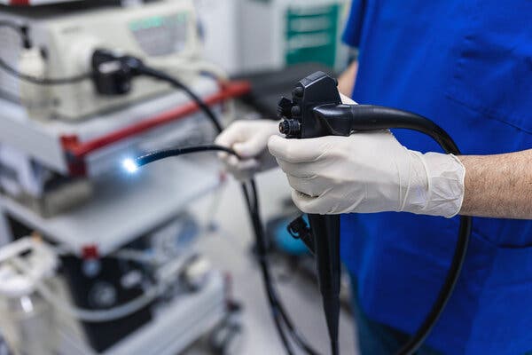 A doctor’s gloved hands holding an endoscope lit at one end for a colonoscopy.