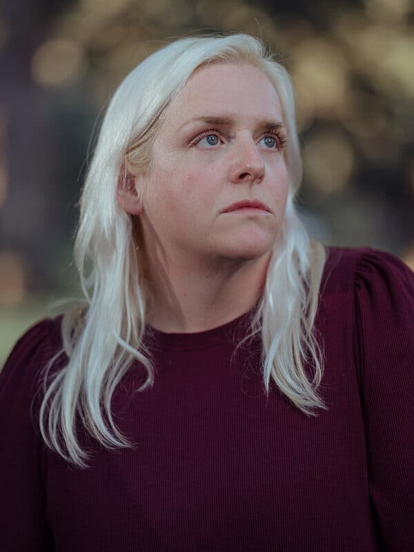 A portrait of Anna Nusslock, who stands in a park and wears a dark red sweater.