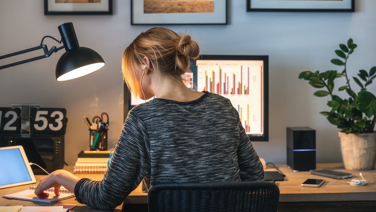 Woman working on computer and digital tablet in her home office during pandemic.