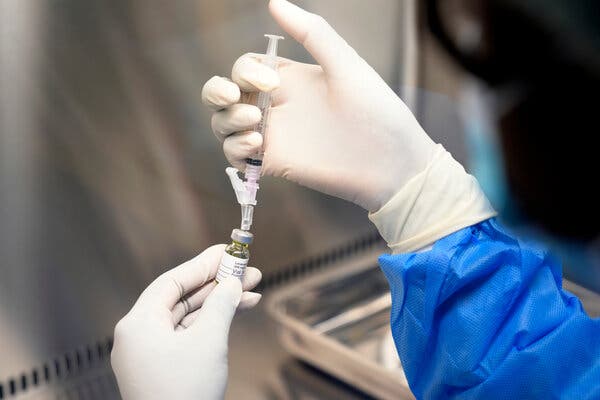 A close-up view of a pair of gloved hands working with a syringe and vial of a liquid drug in a lab setting.