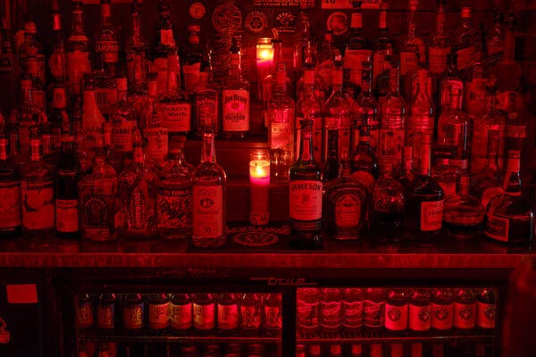 A bar bathed in red light and filled with dozens of bottles of liquor and beer.