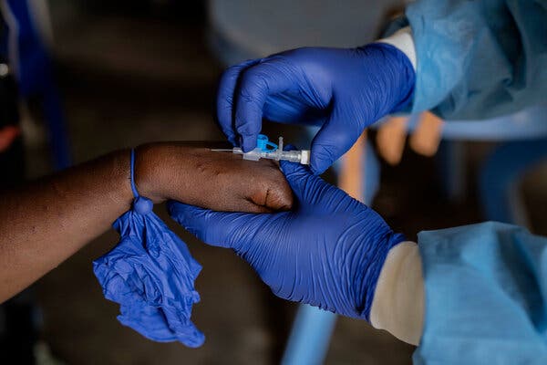 A medical worker’s hand, in blue gloves, performs an injection on an outstretched hand.