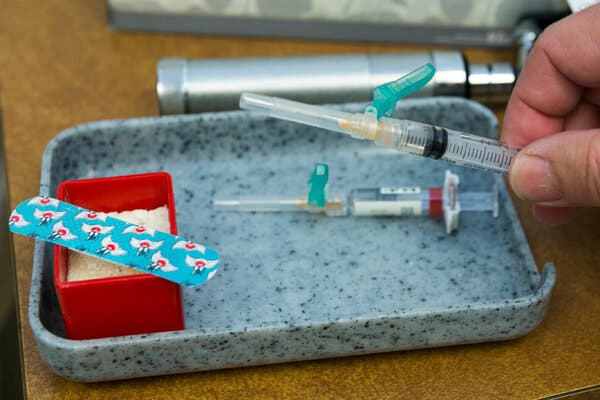 A close-up view of a small tray with two pediatric vaccines and a cartoon bandage in a clinic.