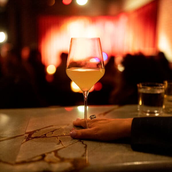 A hand rests on the stem of a glass of wine on a bar.