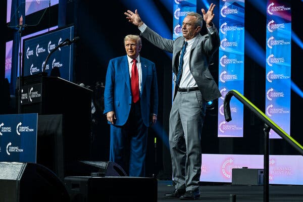 Robert F. Kennedy Jr. raises his arms to greet the crowd while onstage with Donald Trump at a campaign event.