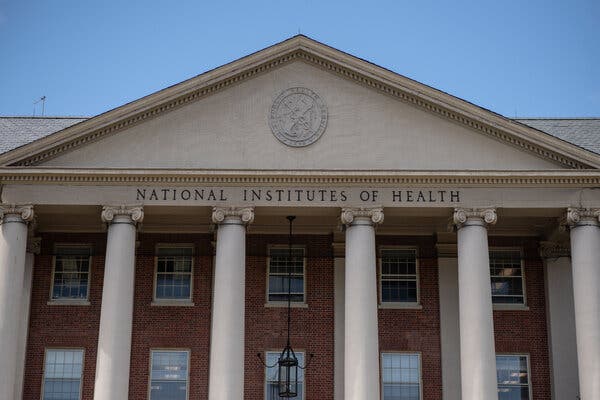 The facade of a brick building with Roman columns. A sign says “National Institutes of Health.”