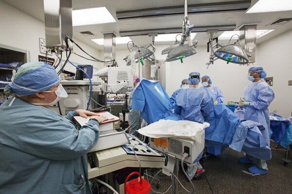 Surgeons in blue smocks, hair coverings, masks and gloves perform final checks before beginning a surgery in an operating room.