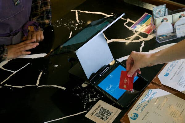 A close-up view of a customer paying at a computer card reader at a coffee shop at a counter.