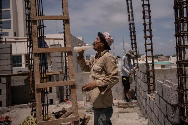 A construction worker takes a sip of milky liquid from a plastic bottle while at a work site in Veracruz, Mexico, on a bright day.