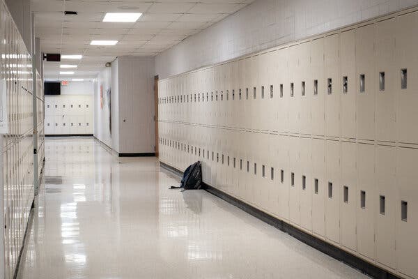 A clean, cream-colored hallway lined with lockers at Neosho High School. The hallway is empty except for a single backpack resting against a locker.