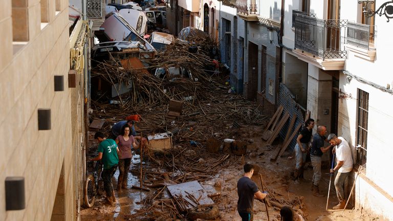 People work to clear a mud-covered street with piled up cars in the aftermath of torrential rains that caused flooding, in Paiporta, Spain, October 31, 2024. REUTERS/Eva Manez