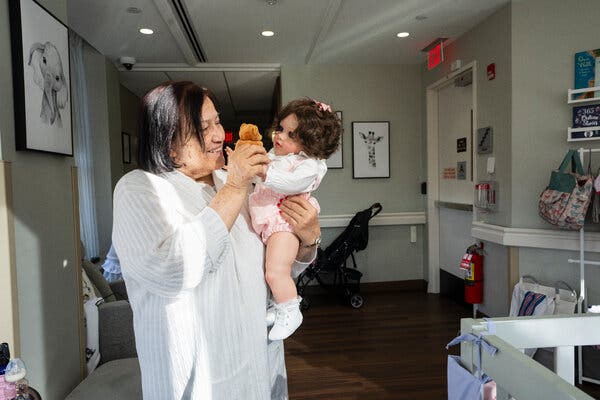 01sci-span-01-gjmb-articlelarge Wilma Rosa smiles as she holds a baby doll and plays with its wrist in a nursery setting, which includes strollers and a crib.